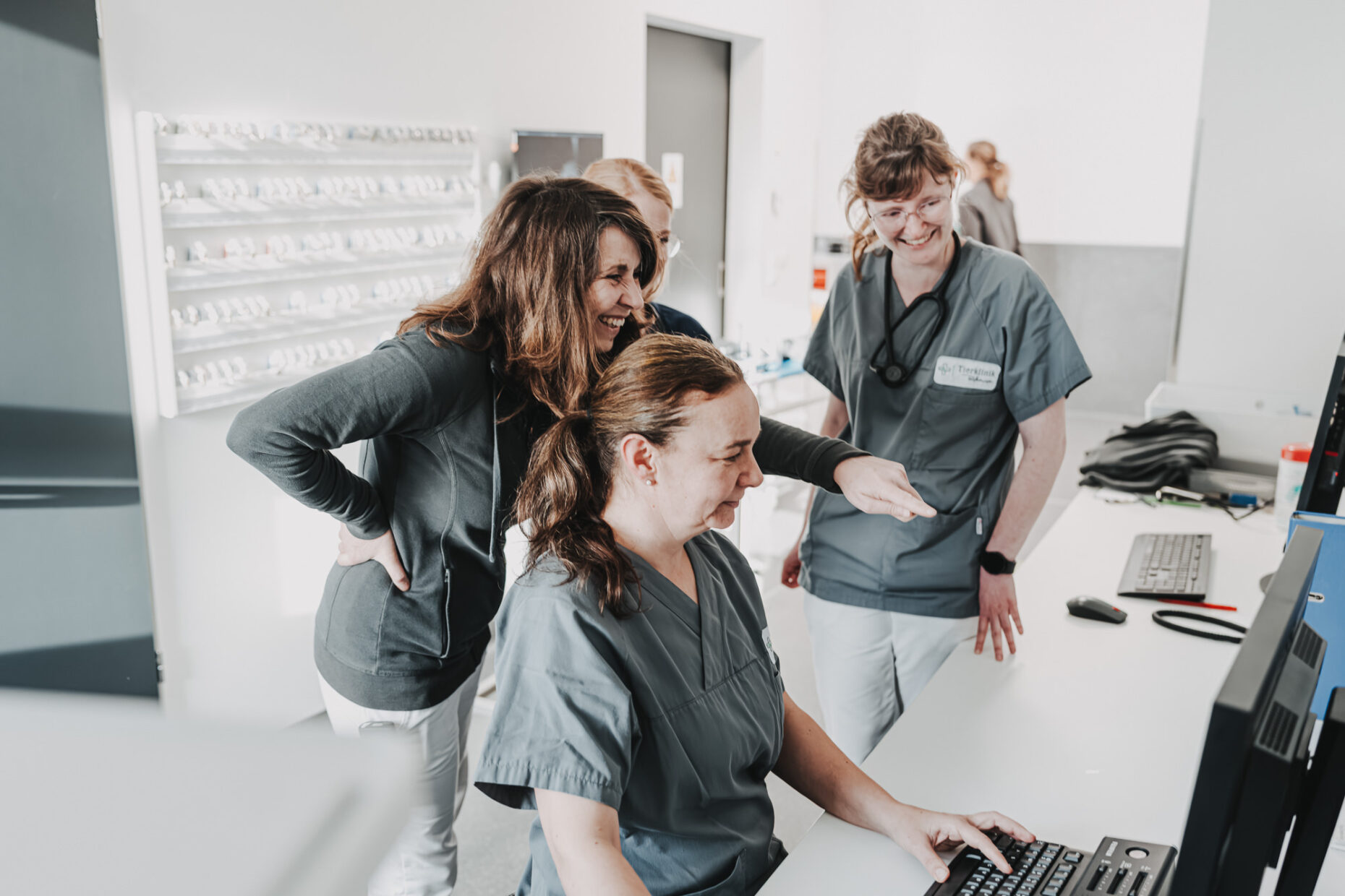 Drei Mitarbeiterinnen der Tierklinik Posthausen stehen und sitzen lächelnd zusammen an einem Computerarbeitsplatz.