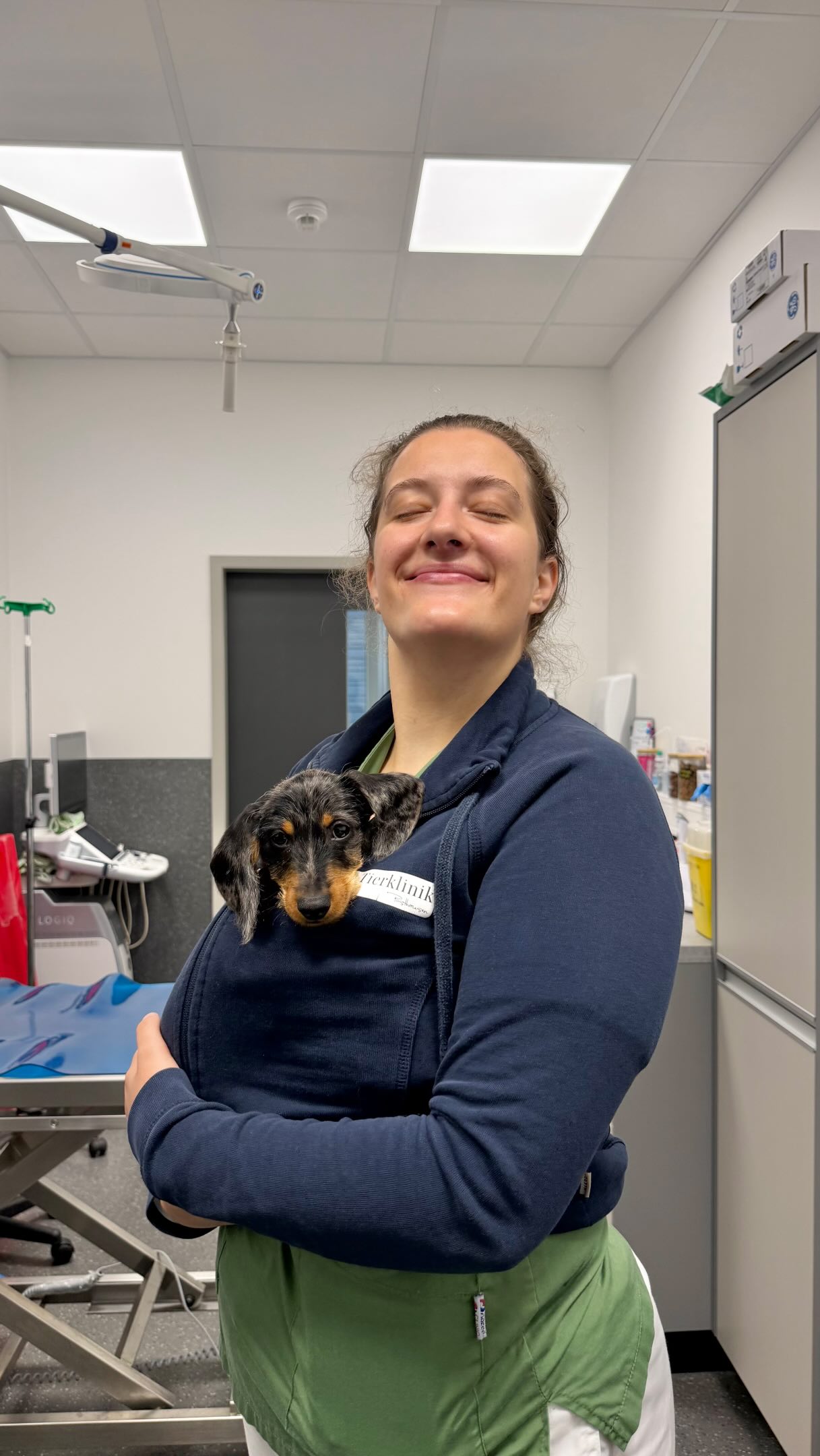 Eine Mitarbeiterin der Tierklinik Posthausen lächelt mit geschlossenen Augen und hält einen Welpen in ihrem Pullover.